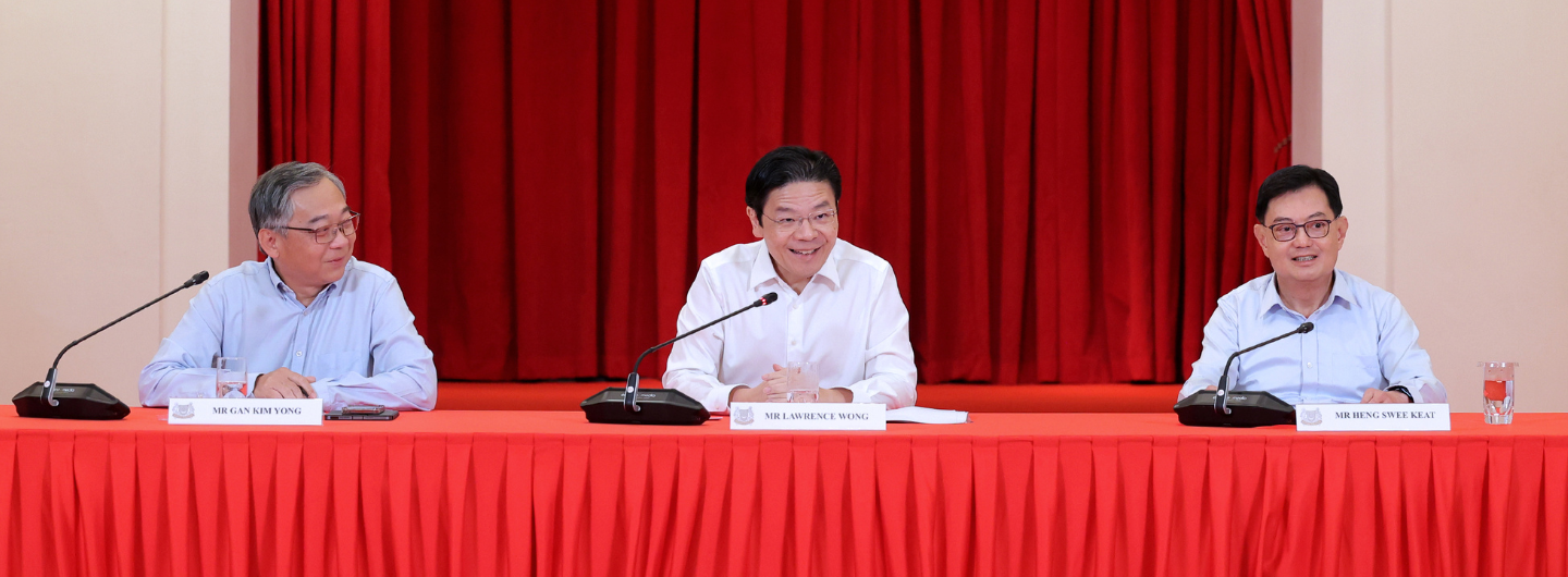 Three men at a red table with microphones in front of a red curtain.